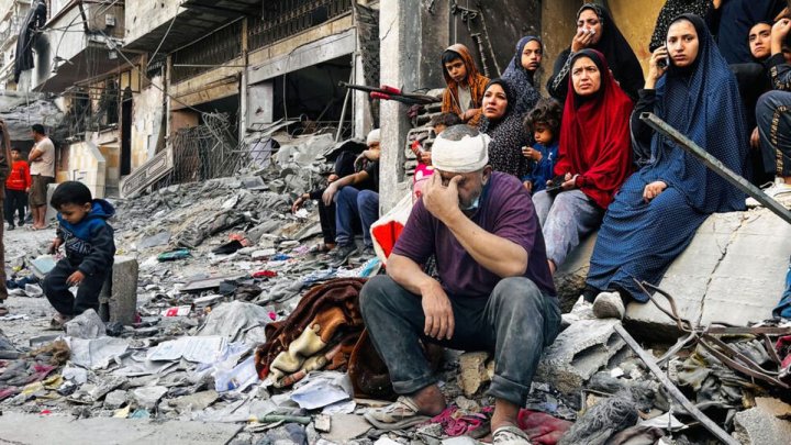 Palestinas y palestino sentados al costado del edificio atacado por Israel el 29/10/24 en Beith Lahiya. Foto: AFP