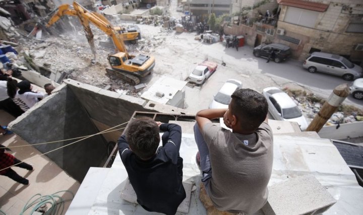 Niños palestinos observan cómo excavadoras israelíes demuelen un bloque de apartamentos palestino supuestamente por no estar autorizado en Jerusalén Este el 1 de mayo de 2018 [Mostafa Alkharouf/Agencia Anadolu]